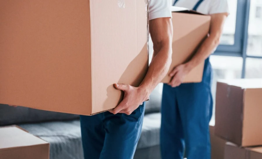 with-boxes-in-hands-two-young-movers-in-blue-uniform-working-indoors-in-the-room.jpg